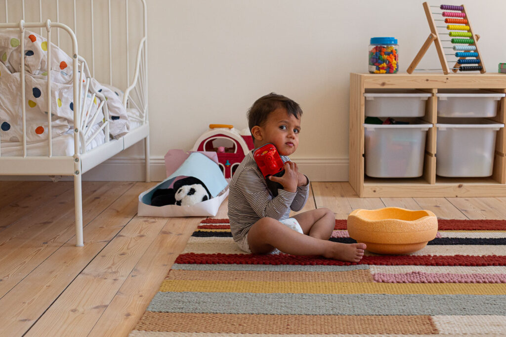 Kind spielt auf Teppich mit Montessori-Spielzeug im Kinderzimmer