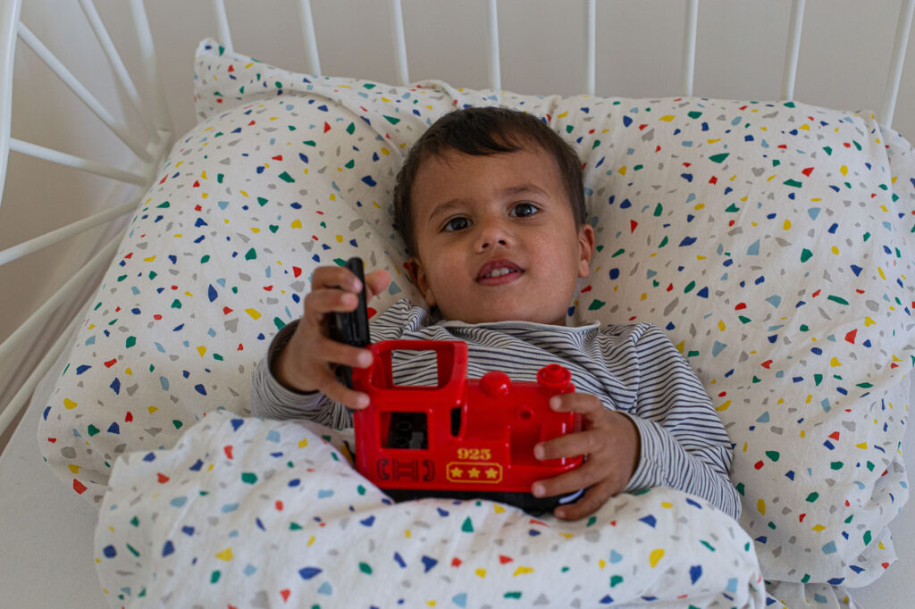 Dokumentarisches Familienfoto: Kind liegt im Bett mit Spielzeug