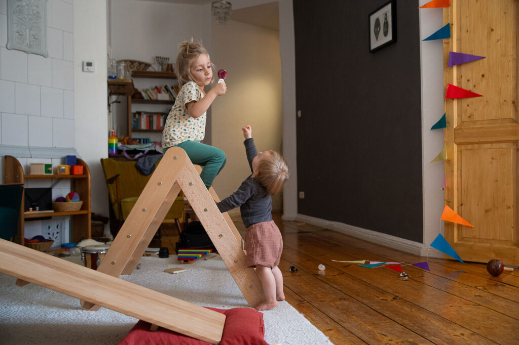 Kind sitzt auf Kletterdreieck mit Eis in der Hand, kleineres Kind streckt sich zum Eis hin, Familienfotos Esslingen