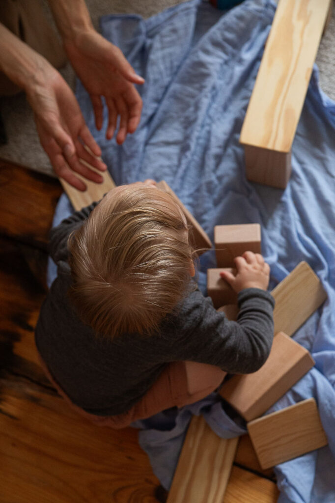 Blick von oben auf ein spielendes Kind, Hände der Mutter ragen ins Bild, Dokumentarische Familienfotografie Esslingen