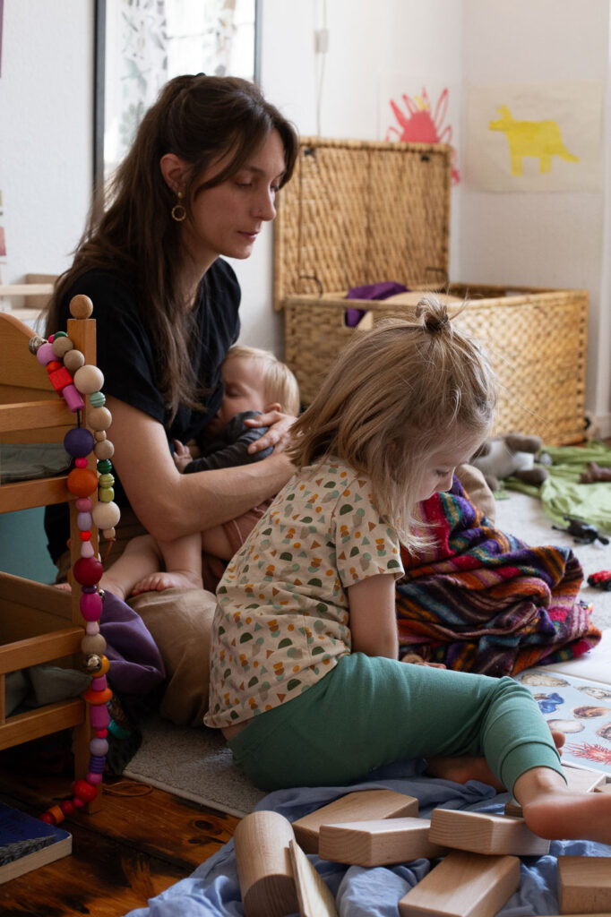 Mama stillt kleines Kind und schaut mit größerem Kind ein Buch an, Dokumentarische Familienfotografie Esslingen