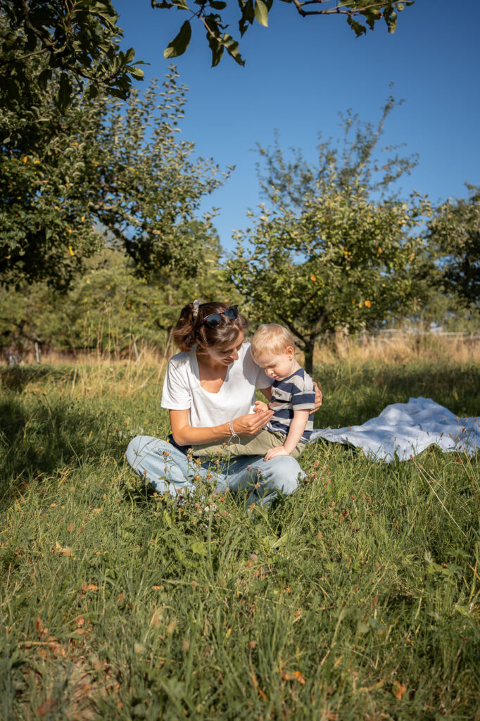 Familienfotoshooting im Grünen: Mutter sitzt mit Kind im Gras