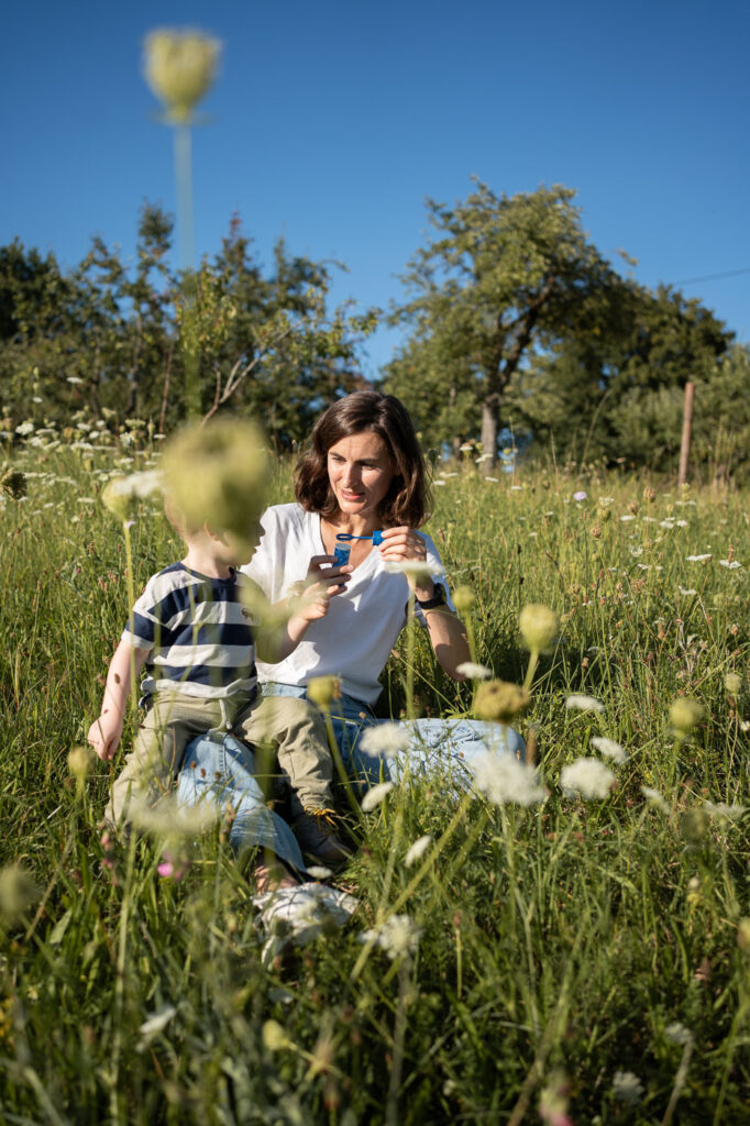 Natürliche Aufnahme: Mutter sitzt mit Kind im Gras, Sommer-Shooting