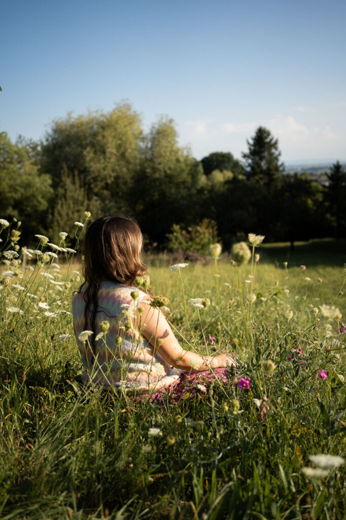 Schwangere Frau genießt die Sonne, sitzt im hohen Gras, Hände am Bauch