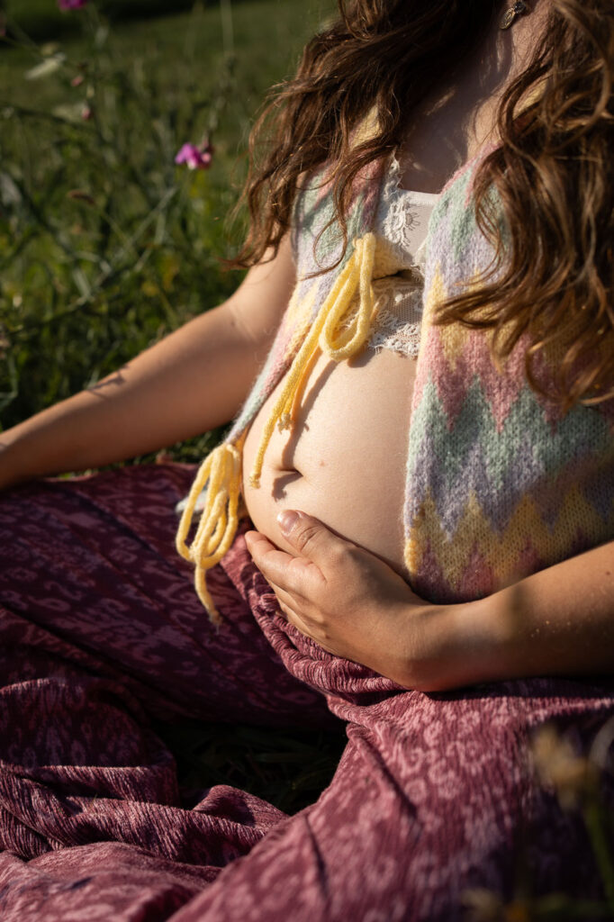 Fotoaufnahme einer Schwangeren im Grünen, Hände am Bauch