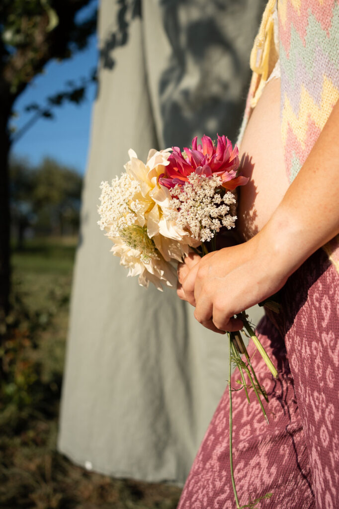 Nahaufnahme: Schwangere Frau hält Blumenstrauß, warme Lichtstimmung