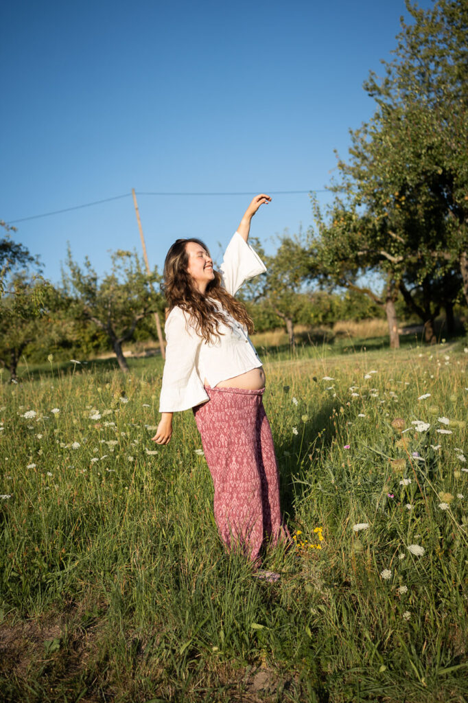 Schwangere Frau tanzt barfuß durchs Gras, Selbstliebe mit Babybauch