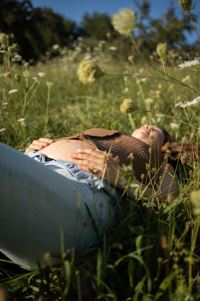 Detailaufnahme: Schwangere liegt im Grünen, Hände am Bauch