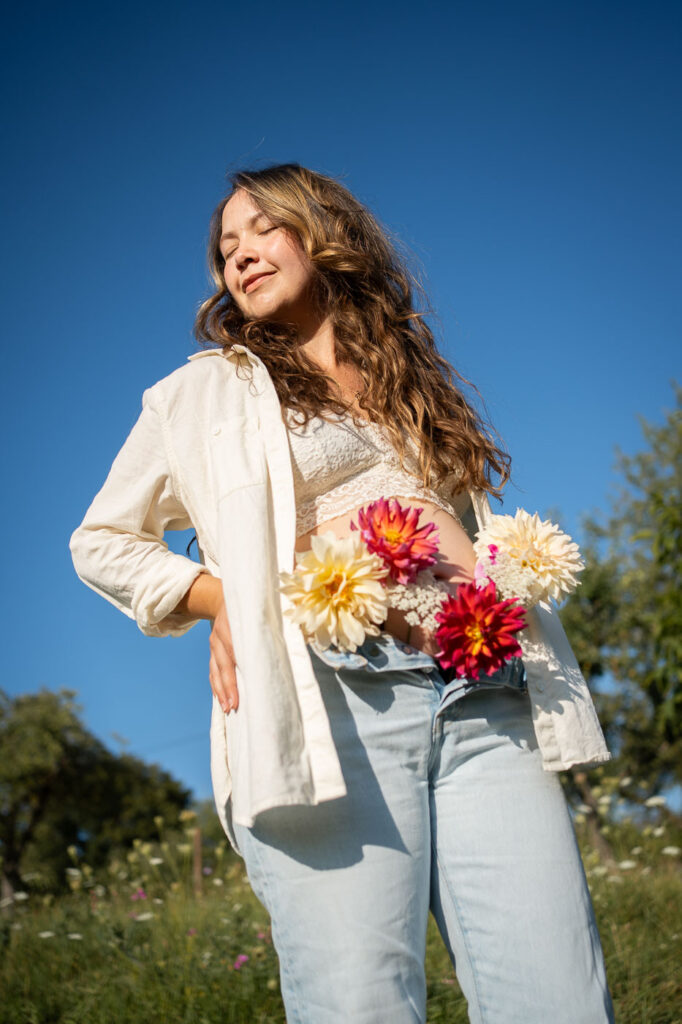 Strahlendes Schwangerschafts-Porträt mit Blumenstrauß vor blauem Himmel