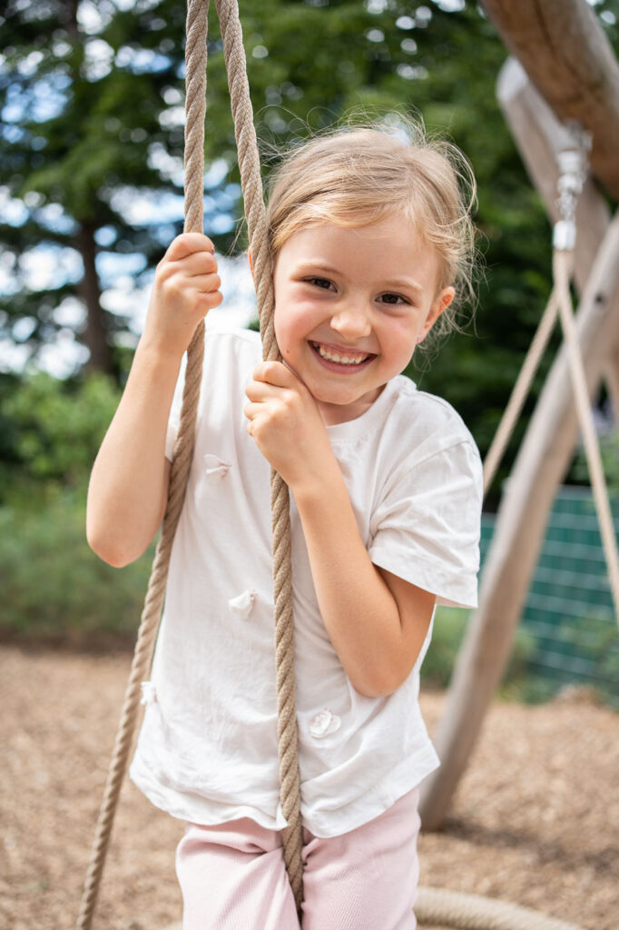 Mädchen auf Schaukel lacht in Kamera, natürliche Kindergartenfotografie Esslingen