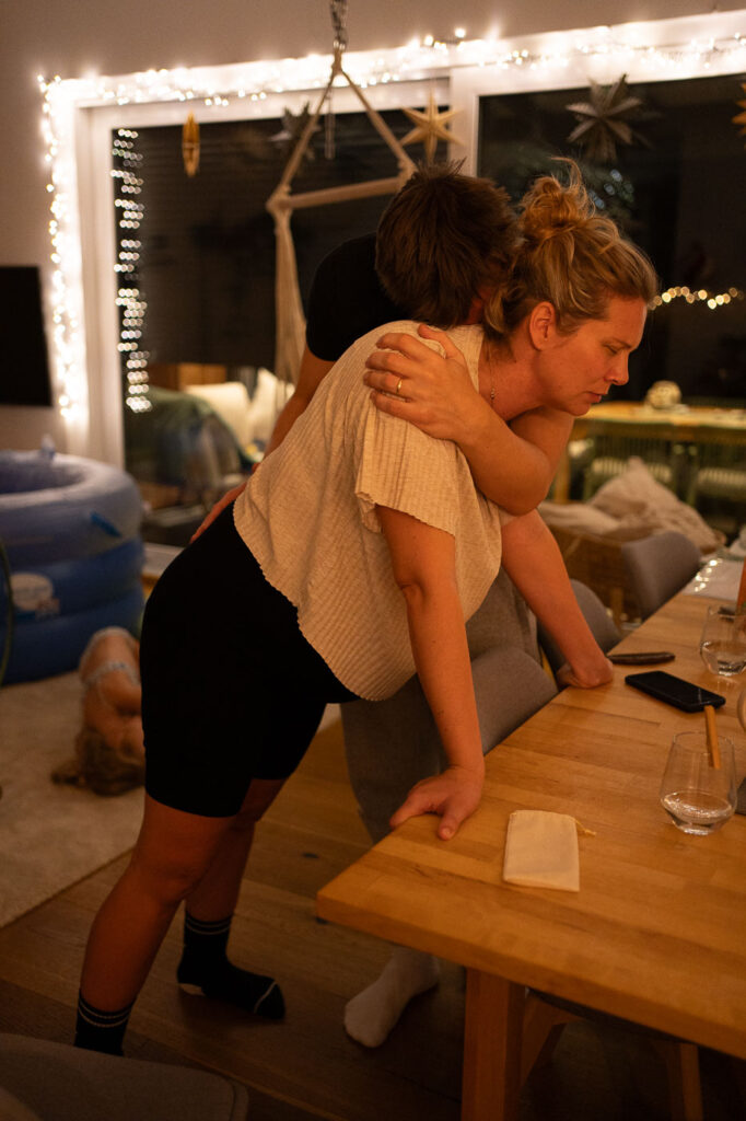 Frau stützt sich auf Tisch, Mann umarmt sie, Sensible Geburtsfotografie Hausgeburt Esslingen