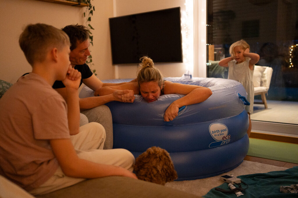 Frau im Geburtspool umringt von Familie, Geburtsfotografie Esslingen, Geburtsreportage Stuttgart