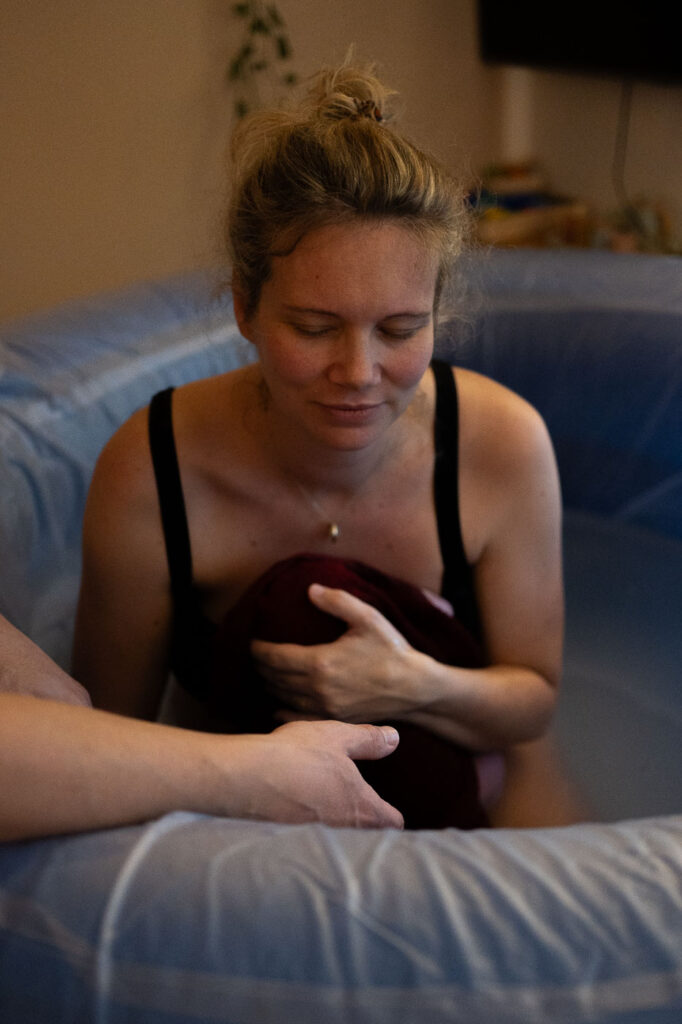 Frau hält Neugeborenes mit geschlossenen Augen im Geburtspool, Geburtsfotografie Stuttgart